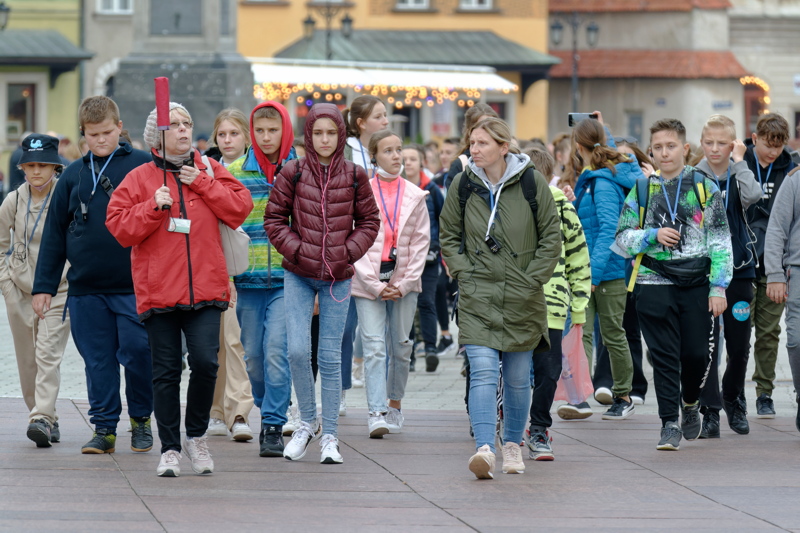 A large group of young tourists exploring a city center, dressed in casual, practical clothing like jackets and hoodies